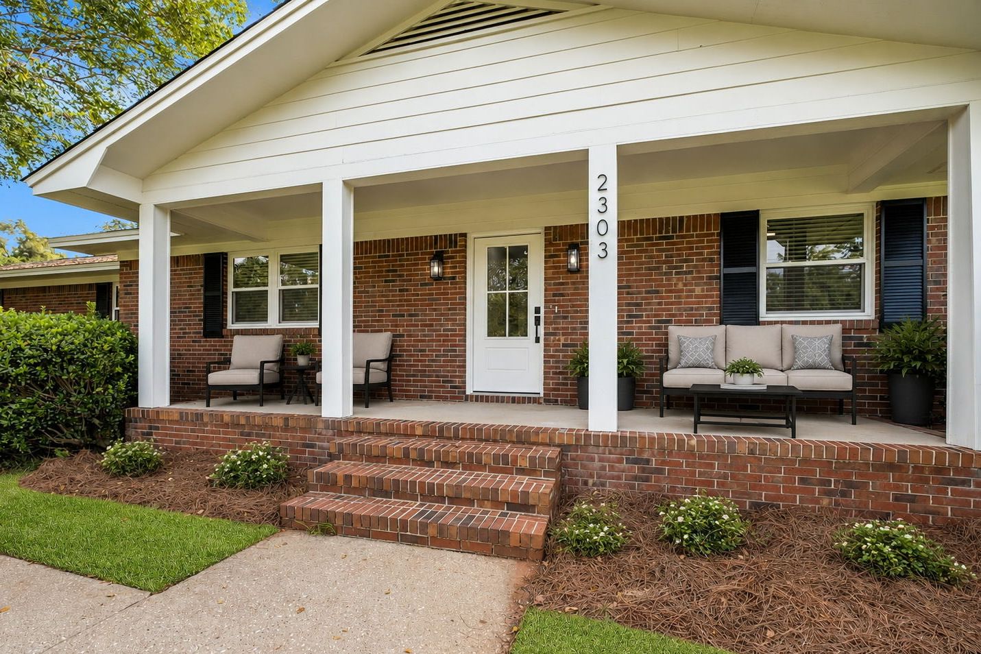 Covered front porch with brick steps and the house number, virtually staged with outdoor seating