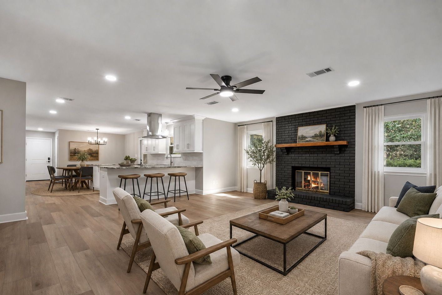 Open living room and kitchen, virtually staged, with a black-painted brick fireplace under a wood mantel