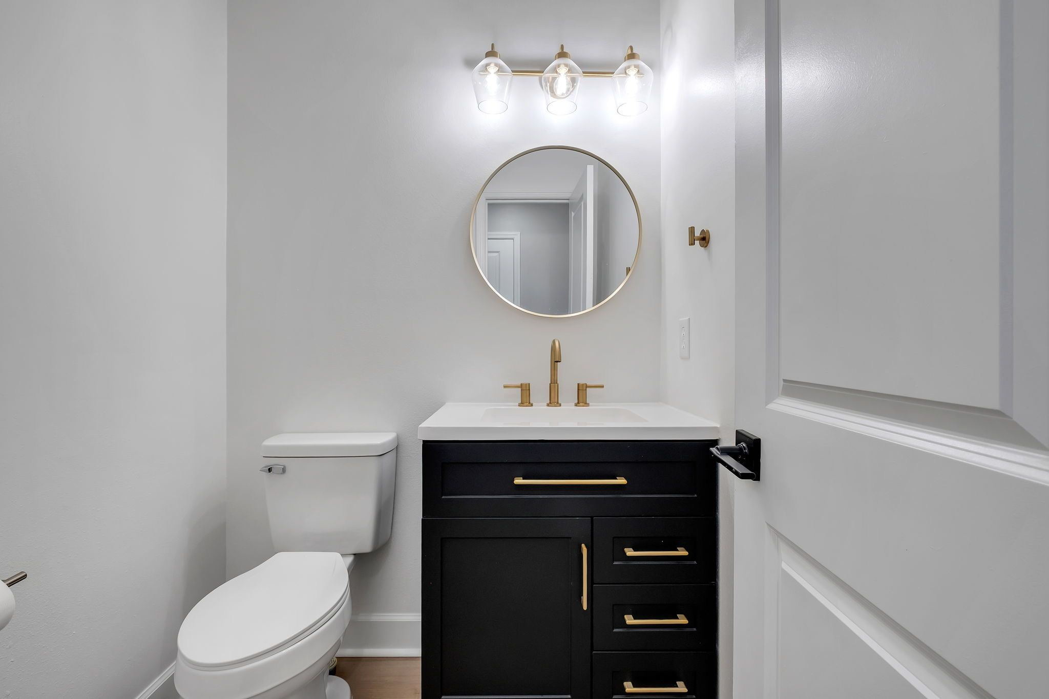 Half bathroom with a black vanity, brass fixtures, and a round mirror